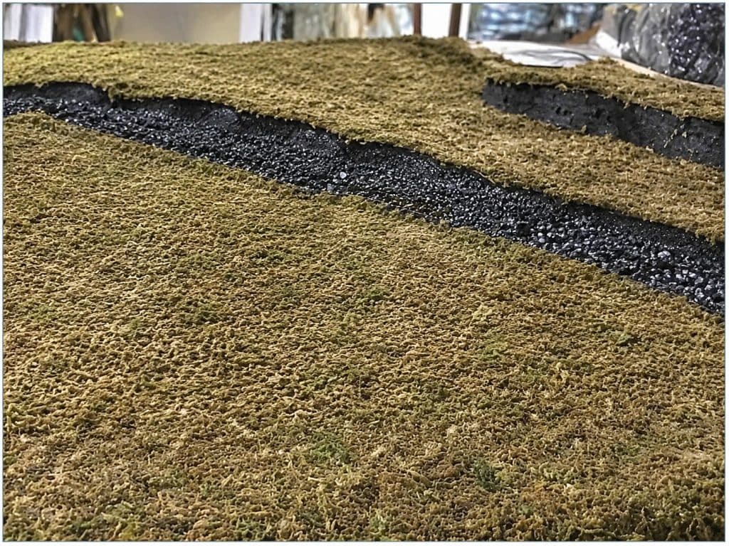 Halloween village ground cover made with moss-like material and dark gravel over raised foam-board levels.