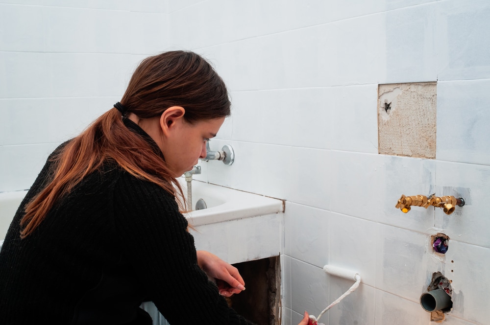 Girl priming and painting old tiles in the bathroom