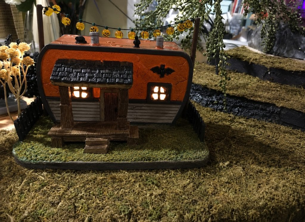 Halloween village house arranged on a raised landscaped level with ground cover and trees.