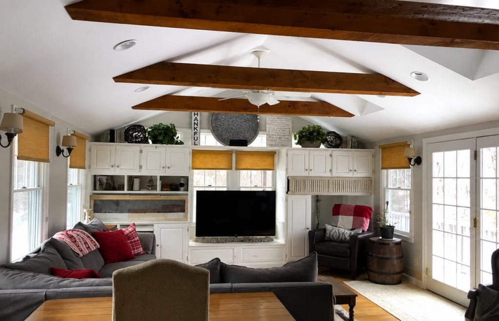 Living room with built-in cabinets, gray sectional sofa, armchair, windows, French doors, and exposed wood ceiling beams.